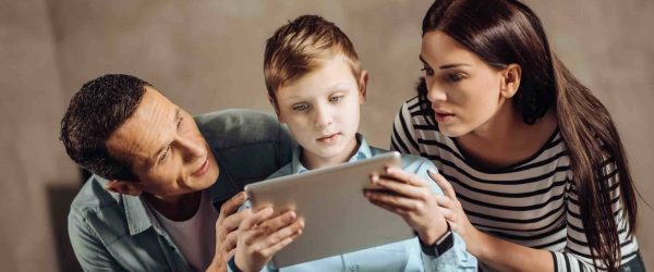 Vater und Mutter hocken hinter Kind mit Tablet in der Hand